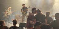Im Vordergrund sitzende und stehende Fans von Pisse. Auf der Bühne links Ronny am Bass, rechts Ronny an der Gitarre, im Hintergrund Nebel.