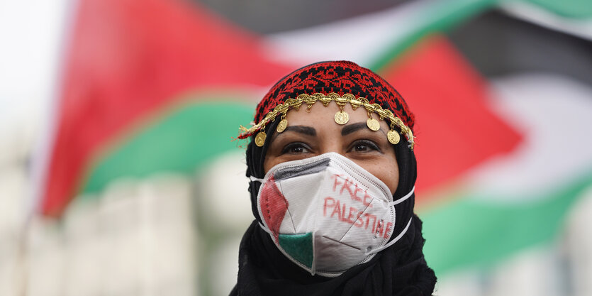 Demonstrantin mit "Free Palestine"-Mund-nasen-maske vor palästinensischen Fahnen