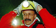 Jürgen Trittin trägt einen roten Overall und einen Schutzhelm mit einer Stirnlampe