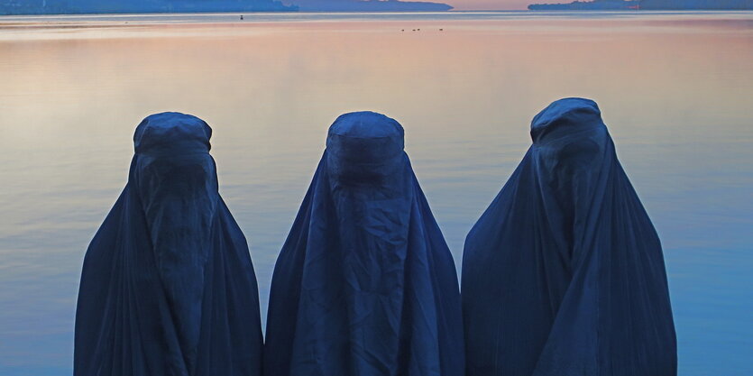 Drei Personen mit burkas vor einem See