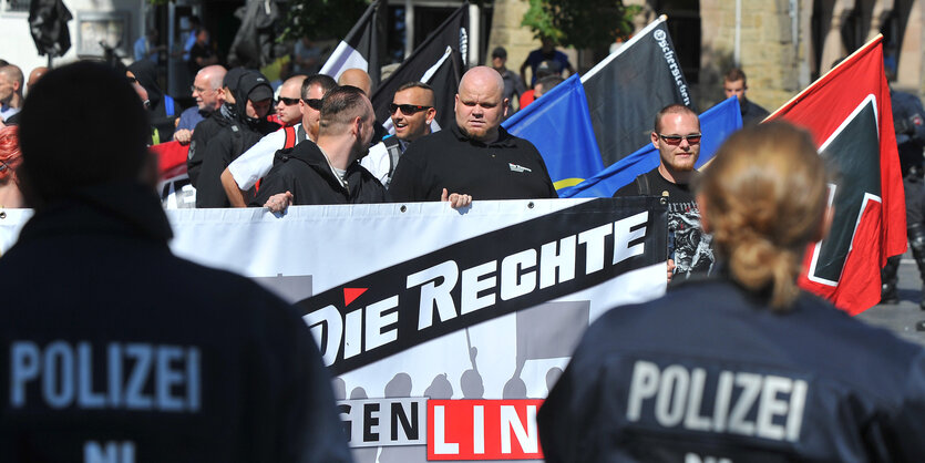 Neonazis halten ein großes Transparent und Fahnen, im Vordergrund die Silhouetten von PolizistInnen