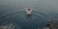 Eine Frau im Badeanzug steht in einem See, von hinten aufgenommen