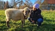 Die Autorin Hilal Sezgin hockt neben einem ihrer Schafe auf einer Wiese. Sie schaut das Schaf lächelnd an.