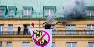 Von einem Balkon im Adlon haben Menschen ein Transparent mit einem durchgestrichenen Dino gehisst; ein Rauchtopf brennt