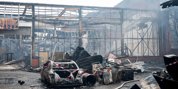 Ein Autowrack und Brandschutt im Stadtteil Rothenburgsort vor den Resten einer abgebrannten Lagerhalle
