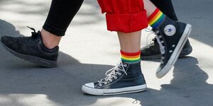 Menschen laufen auf Asphalt, eine Person trägt Turnschuhe und Socken in Regenbogenfarben, Detailaufnahme