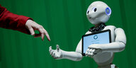 Das Foto zeigt einen weißen Roboter, der nach einer menschlichen Hand greift.