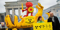 ürgen Trittin (Bündnis 90/Die Grünen), Mitglied des Deutschen Bundestages und ehemaliger Umweltminister, steht neben einer Aktivistin vor einer Dinosaurier-Figur und der roten Sonne, teil des Anti-Atomkraft-Logos, bei einer Aktion der Umweltorganisation G