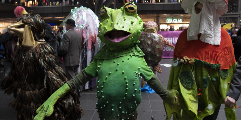 Ein Mensch im Froschkostüm und andere Tierfiguren. Am 15.4.2023 demonstrieren Aktivisten der Umweltschutz-Gruppe Extinction Rebellion mit einem Tanz-Flashmob im Berliner Hauptbahnhof auf das weltweite Artensterben aufmerksam