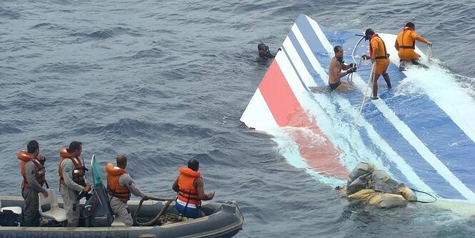 Eine Schlauchbott mit vier Männern, weitere Männer stehen auf der Heckflosse eines abgestürzten Flugzeugs