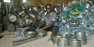 Ein Mitarbeiter von Happy Amos' Unternehmen sitzt inmitten vieler Kochtöpfe grinsend auf dem Boden und ummantelt sie mit Metall