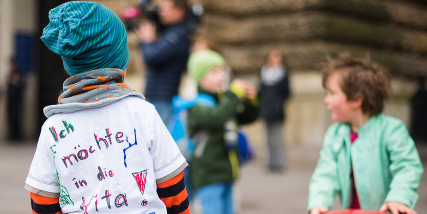 Aufnahme eines Kindes von hinten. Aufschrift auf dem T-Shirt: „Ich möchte in die Kita“