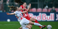 Eine Spielerin von Freiburg und Leipzig grätschen mit ausgestrecktem Bein zum Ball