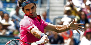 Roger Federer hat die Haare mit einem Stirnband zurückgebunden und spielt gerade einen Ball