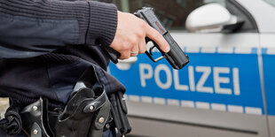 Ein Polizist steht mit gezogener Dienstwaffe vor einem Polizeiwagen.