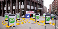 Protest gegen Datenklau: aufgestellte Smartphones mit Whatsapp-Ikon, von denen Leitungen zu einem Facebook-Symbol führen