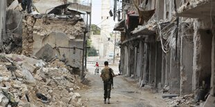 Bewaffneter geht durch eine zerstörte Gasse in Aleppo.