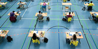 Schüler sitzen an Tischen in einer Turnhalle bei einer Prüfung