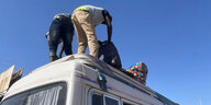Zwei Männer verstauen Gepäckstücke auf dem Dach eines Busses