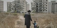 Ein Kind an der Hand eines orthodoxen Juden in einer Neubausiedlung