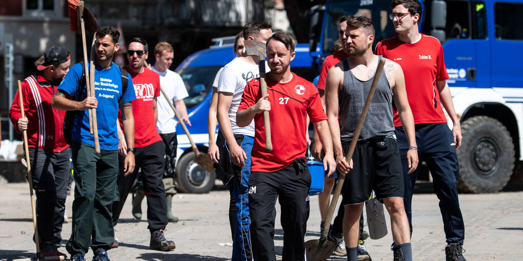 Junge Männer marschieren mit Schaufeln und Eimern zum Aufräumen nach der Flutkatastrophe im Ahrtal.