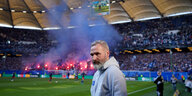 HSV-Trainer Tim Walter in grauen Kapuzenpulli vor der HSV-Fantribüne, von der blauer Rauch aufsteigt