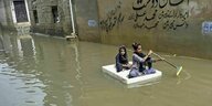 Zwei Kinder paddeln auf einer Art Floß auf einer überfluteten Straße