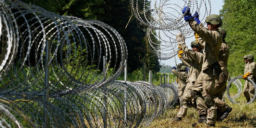 Soldaten verlegen mehrere Rollen Stacheldraht