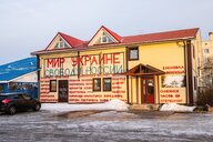 Gelbes einstöckiges Haus mit Antikriegsparolen auf Russisch, etwas schnee und Parkplatz davor