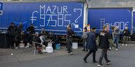 Lkw-Fahrer protestieren und sitzen neben den Lastwagen. In einem Graffiti ist die über 97.000 Euro Geldforderung zu lesen