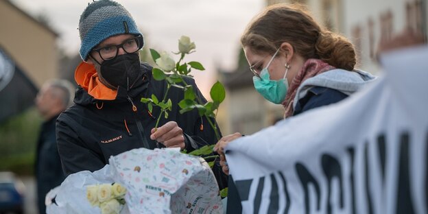 Ein Mann mit Mundschutz verteilt weiße Rosen, eine Frau hält ein Transparent