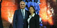 Ein Mann und eine Frau stehen nebeneinander vor einer blauen Statue und rot angeleuchteter Wand