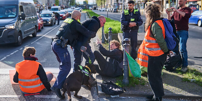 Ein wütender Passant mit Hund geht auf einen Mann los, der neben den Sitzblockierern ist und wird von der Polizei zurückgehalten