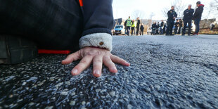 Eine auf der Straße festgeklebte Hand, im Hintergrund Polizei