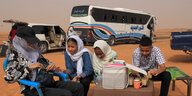 Vier Menschen, darunter drei Jugendliche in der Wüste, hinter ihnen Busse