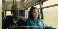 Ein Mann und eine Frau sitzen im Bus nebeneinander. Draußen zieht die Landschaft vorbei