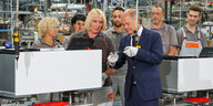 Bundesklanzler Scholz befestigt eine Schraube an einer Wärmepumpe, umstanden von Mitarbeitern des Unternehmens Viessmann