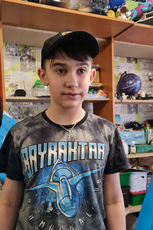 Max, ein 13jähriger Junge, steht mit Basecap und schwarzem Shirt vor seinen Bildern