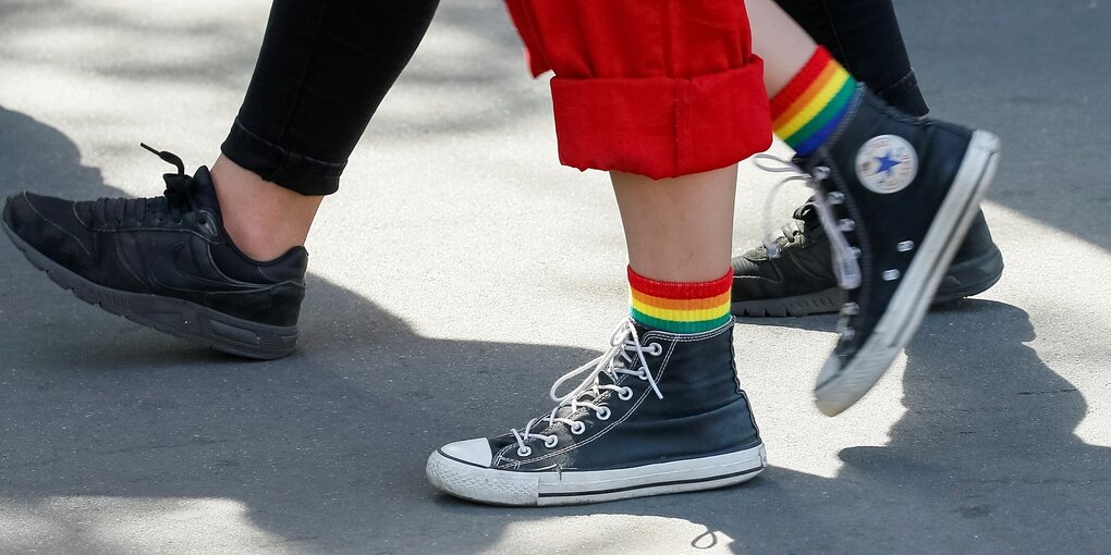 Menschen laufen auf Asphalt, eine Person trägt Turnschuhe und Socken in Regenbogenfarben, Detailaufnahme