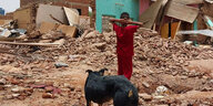 Ein Mensch in roter Kleidung und ein Hund stehen vor den Ruinen eines hauses