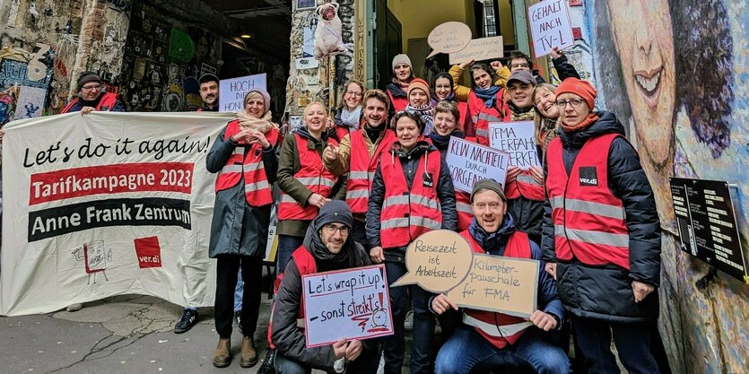 Gruppenbild der Mitarbeiter des Anne frank Zentrums in Verdi-Warnwesten und mit Transparent