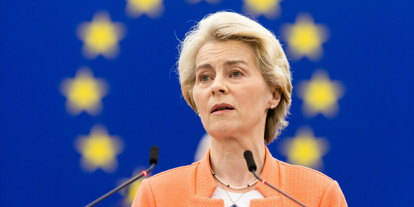 Ursula von der Leyen spricht vor einer Wand mit EU-Flagge.