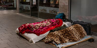 Zwei Personen liegen unter Decken auf Matratzen auf einem Fußweg