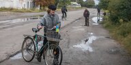 Ein mann schiebt ein fahrrad über die Straße, am Lenker ist ein Ukraine-Fähnchen befestigt