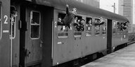 Junge Männer winken aus dem abfahrenden Zug im Bahnhof
