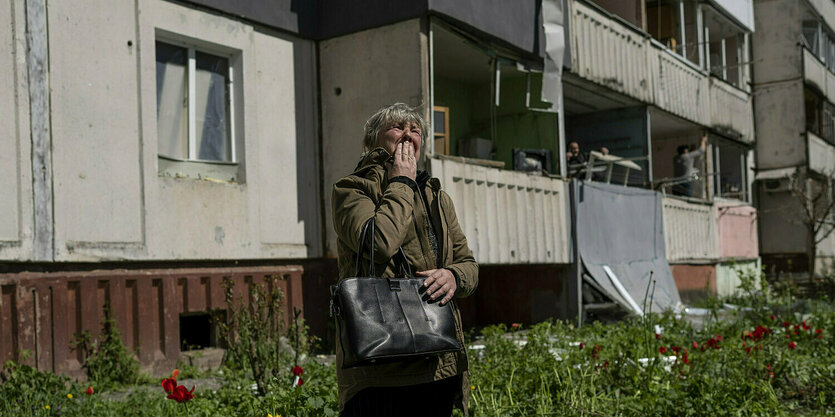 Eine Frau steht vor einem Wohnblock und hält ihre Hand vor den Mund