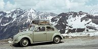 Ein VW Käfer mit dachgepäckträger vor Alpenkulisse