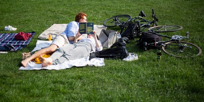 Eine Frau liegt auf einer Wiese und liest das Buch "Noch wach" von Benjamin von Stuckrad Barre