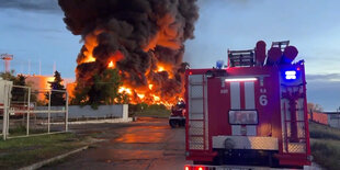 Eine Flammen- und Rauchsäule. davor ein Einsatzwagen der Feuerwehr