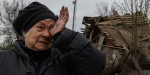 Eine Frau weinend vor ihrem zerstörten Haus